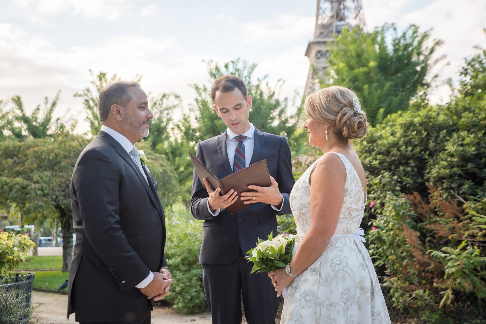 A couple is gazing at each other while officiant Jean-Sebastien reads the ceremony to them in a Parisian park