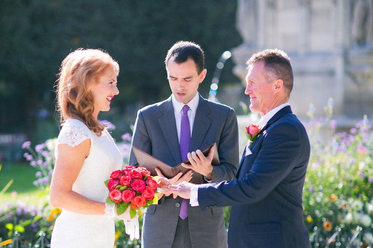 A couple eloping in a garden of Paris is holding hands with a rose bouquet as officiant Jean-Sebastien is celebrating the ceremony